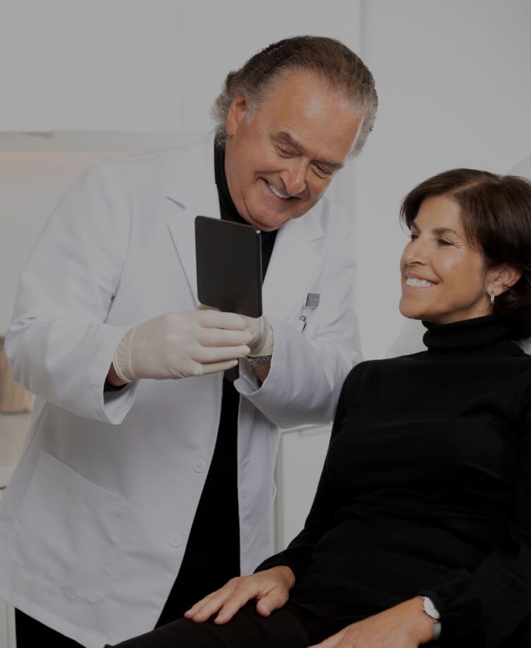 Dr Pierre Rochon, dentiste, tenant un miroir dans sa main afin que sa patiente assise à ses côtés puisse voir son sourire