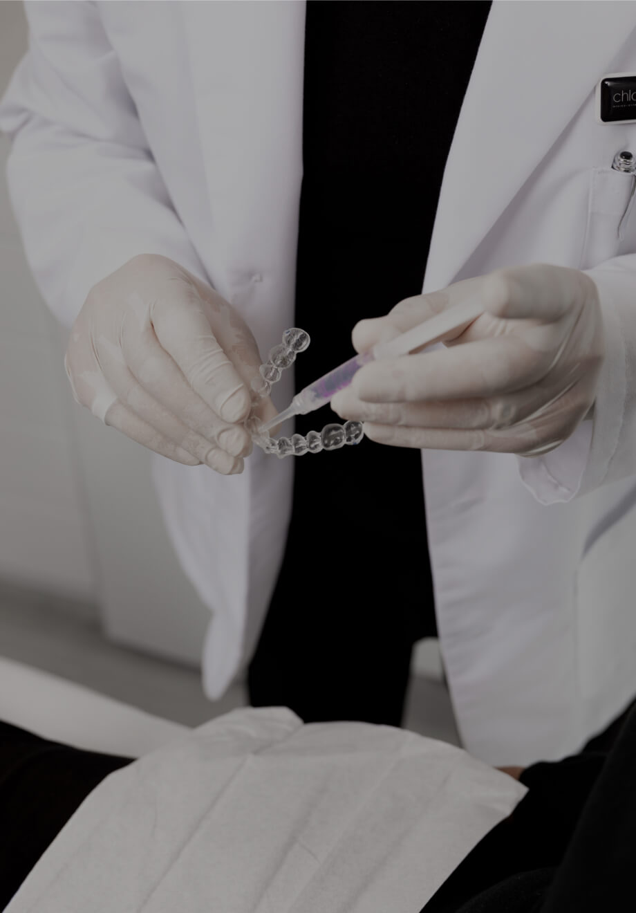 Le dentiste de la Clinique Chloé montrant à une patiente comment remplir les gouttières d'agent de blanchiment dentaire