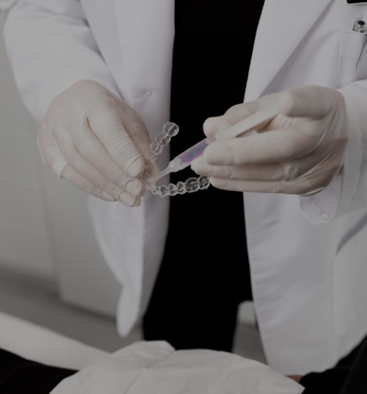 Le dentiste de la Clinique Chloé montrant à une patiente comment remplir les gouttières d'agent de blanchiment dentaire