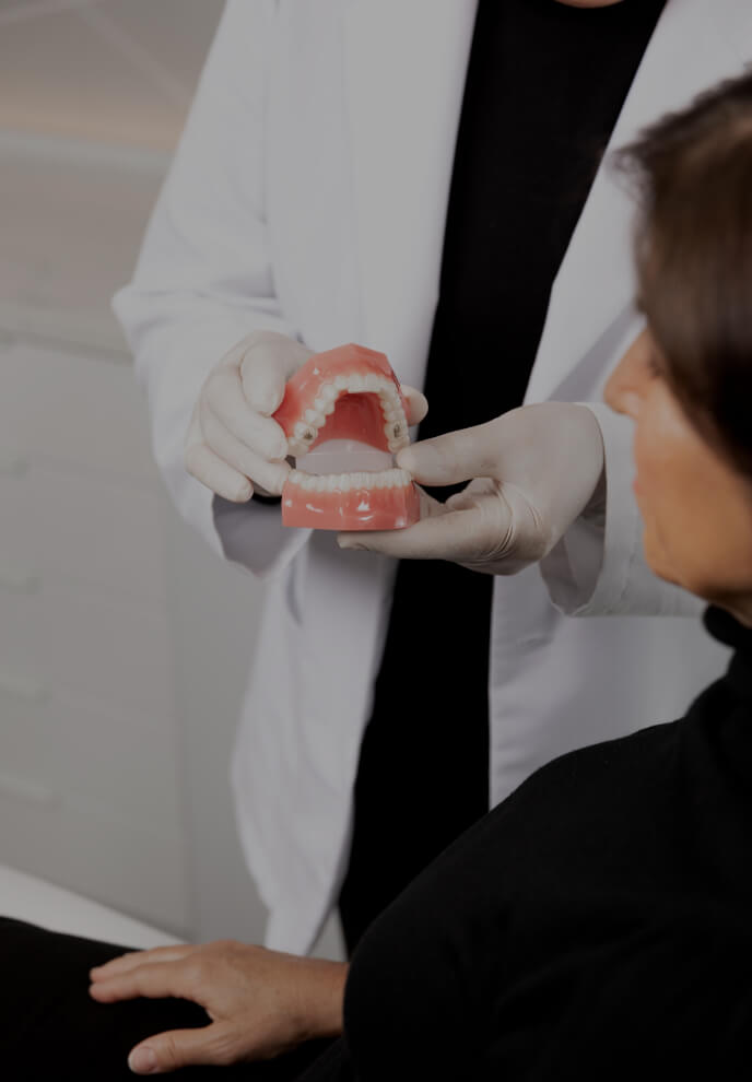 The dentist at Clinique Chloé holding dentures in his hands and explaining the Invisalign treatment to a female patient
