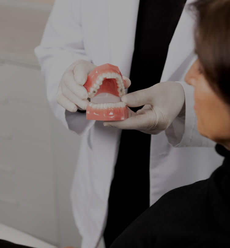 The dentist at Clinique Chloé holding dentures in his hands and explaining the Invisalign treatment to a female patient