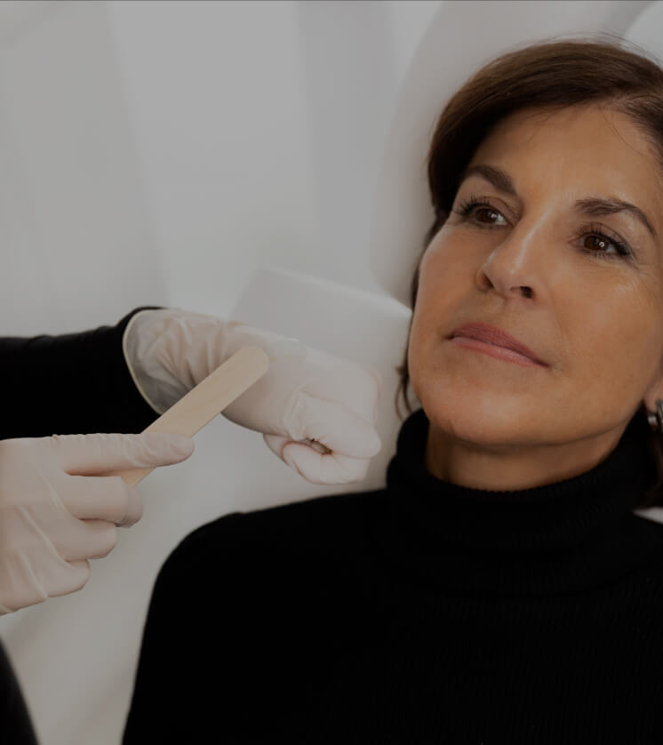 A Clinique Chloé technician applying numbing cream to a patient's face with a stick before a fractional laser treatment