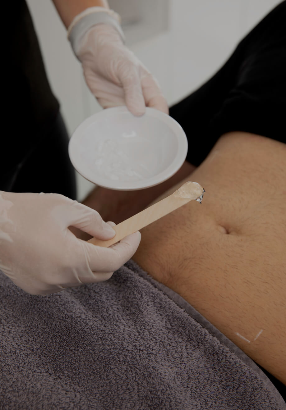 A medico-aesthetic technician from Clinique Chloé applying gel to a patient's abdomen with a wooden stick