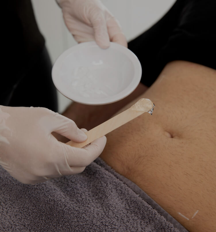 A medico-aesthetic technician from Clinique Chloé applying gel to a patient's abdomen with a wooden stick